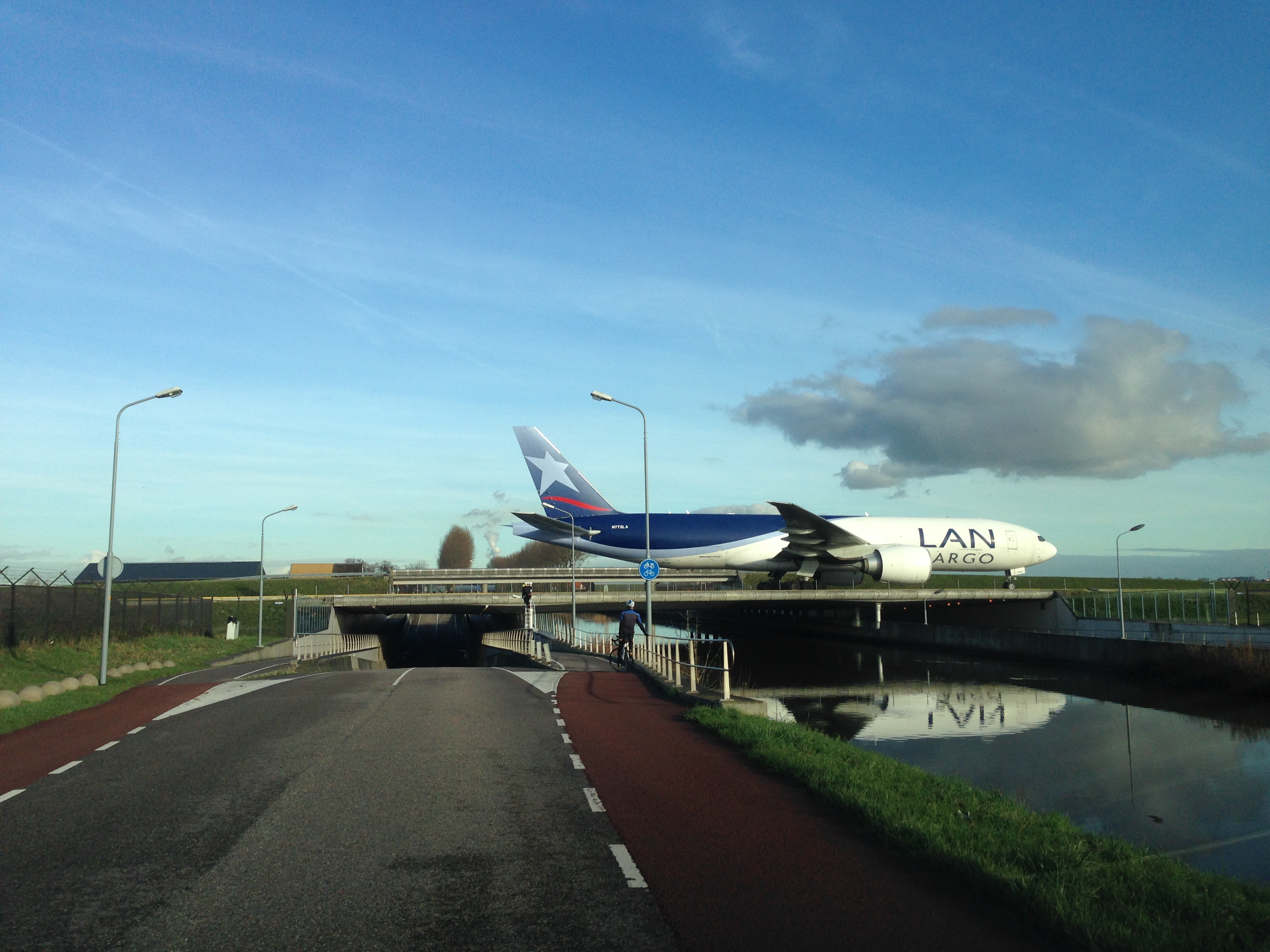 Zijaanzicht van het Hoofdvaartavioduct op Schiphol met een passerend vrachtvliegtuig